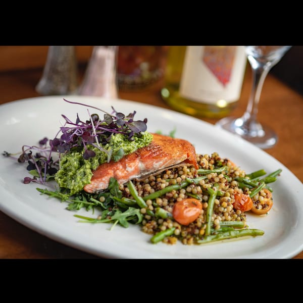 Pan-seared salmon topped with pesto and microgreens, served with pearl couscous, green beans, and tomatoes.