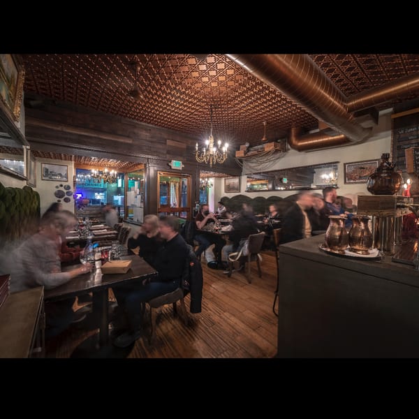 Cozy restaurant interior with blurred patrons dining under a copper ceiling and chandeliers.