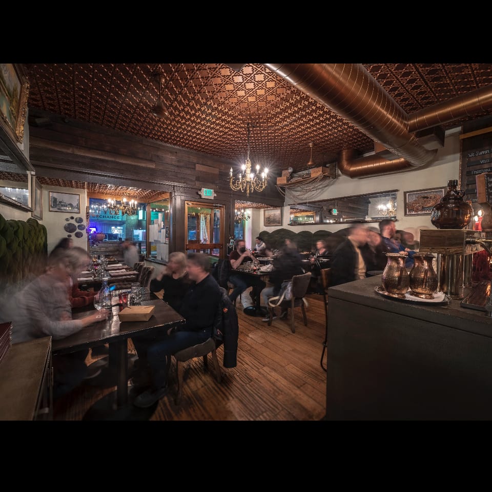 Cozy restaurant interior with blurred patrons dining under a copper ceiling and chandeliers.