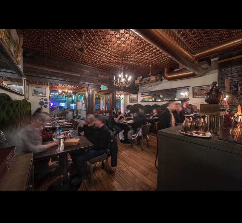 Cozy restaurant interior with blurred patrons dining under a copper ceiling and chandeliers.