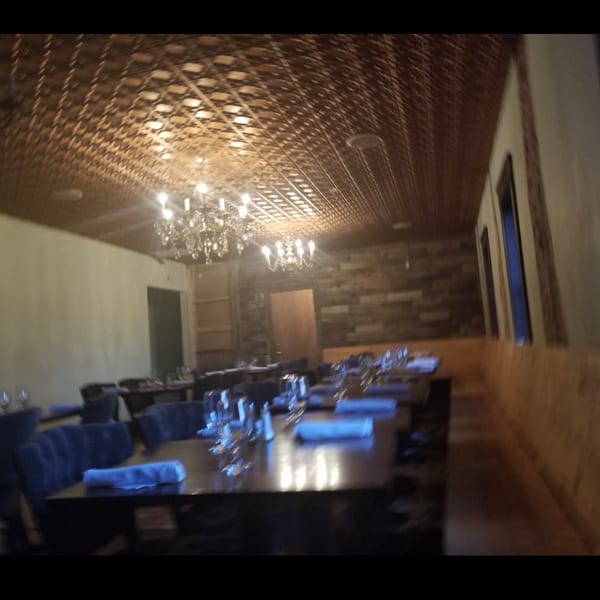 Dimly lit restaurant dining room with set tables, chandeliers, and a unique patterned ceiling.