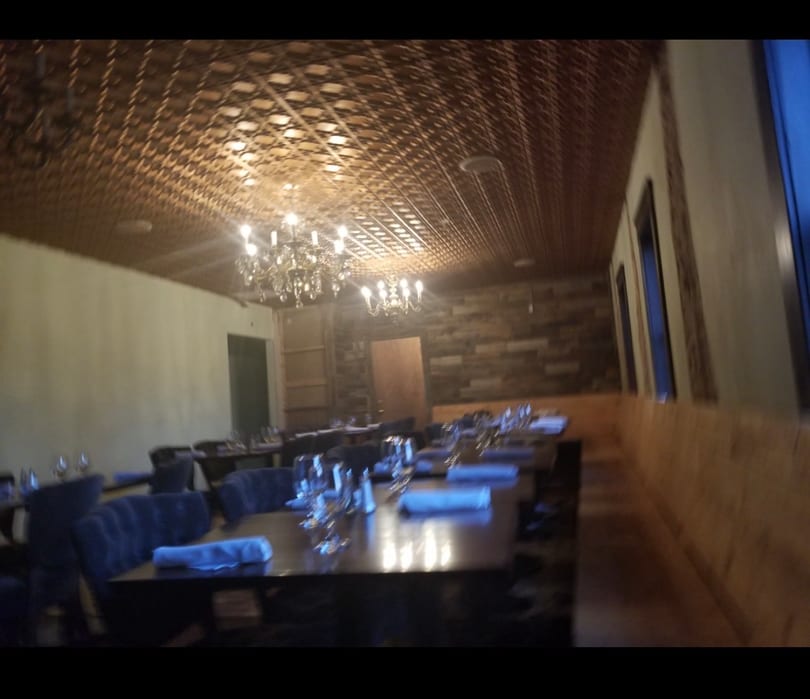 Elegant restaurant dining room with set tables, chandeliers, and a decorative patterned ceiling.