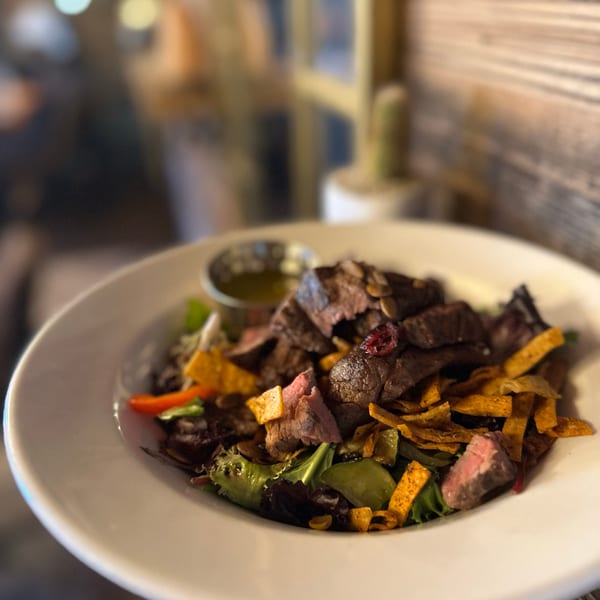 Colorful steak salad with mixed greens, tortilla strips, pumpkin seeds, and a side of dressing.