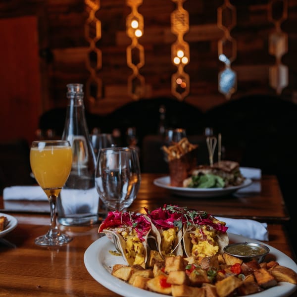 Scrambled egg tacos with red cabbage, home fries, and a mimosa on a restaurant table.