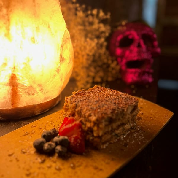 Layered dessert with berries on a wooden board, illuminated by a salt lamp and a pink skull in the background.