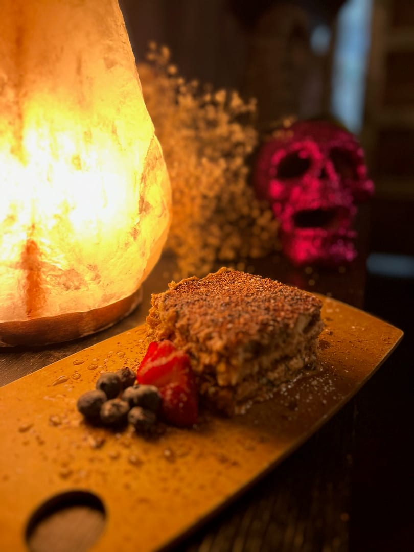 Layered dessert with berries on a wooden board, illuminated by a salt lamp and a pink skull in the background.