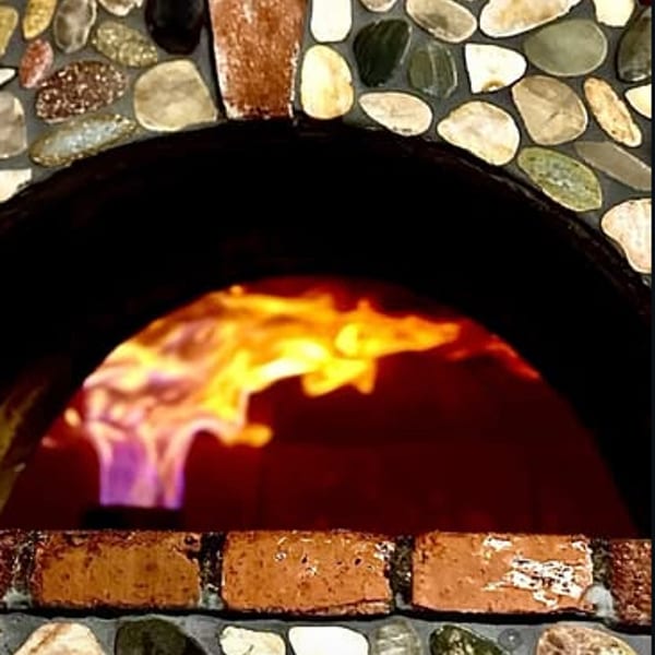 Stone and brick pizza oven with bright flames burning inside.