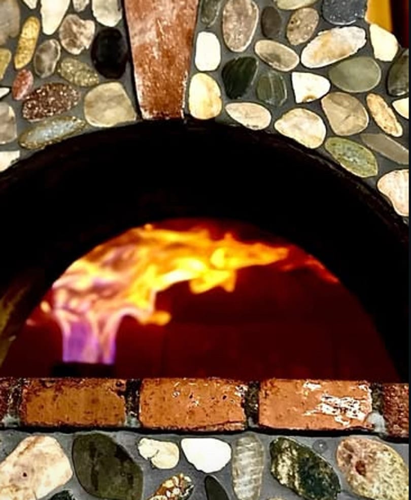 Stone and brick pizza oven with bright flames burning inside.