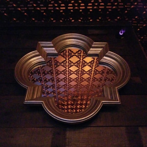 Ornate gold-framed decorative panel with a geometric pattern on a dark wooden wall.