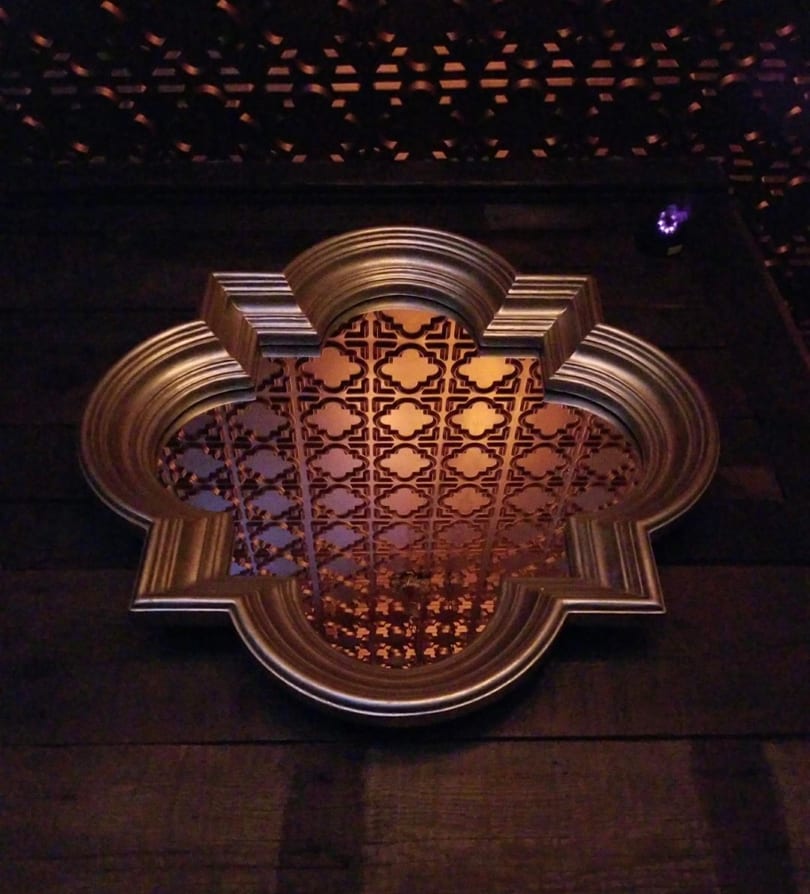 Ornate gold-framed decorative panel with a geometric pattern on a dark wooden wall.