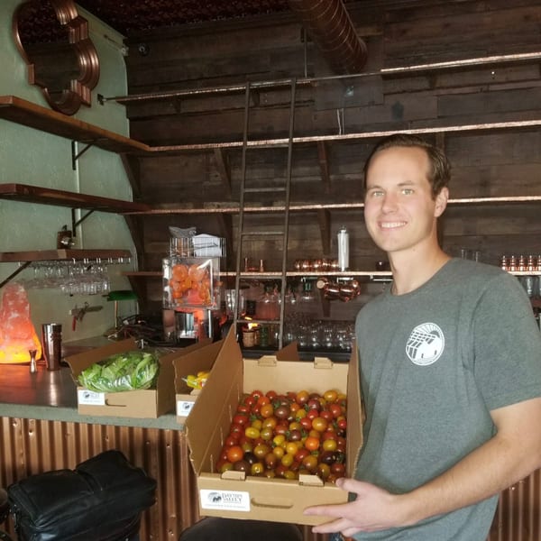 Smiling man holds a box of colorful cherry tomatoes in a restaurant bar.