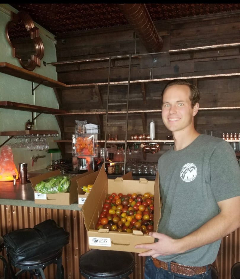 Smiling man holds a box of colorful cherry tomatoes in a restaurant bar.