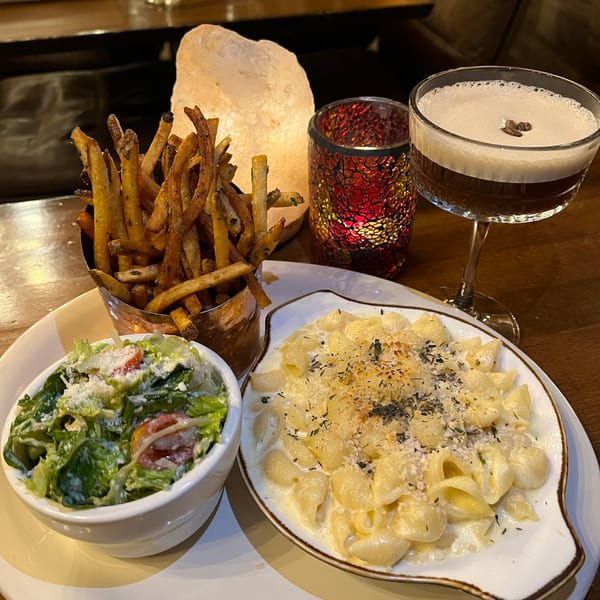 Creamy mac and cheese, crispy fries, fresh salad, and a cocktail on a cozy restaurant table.
