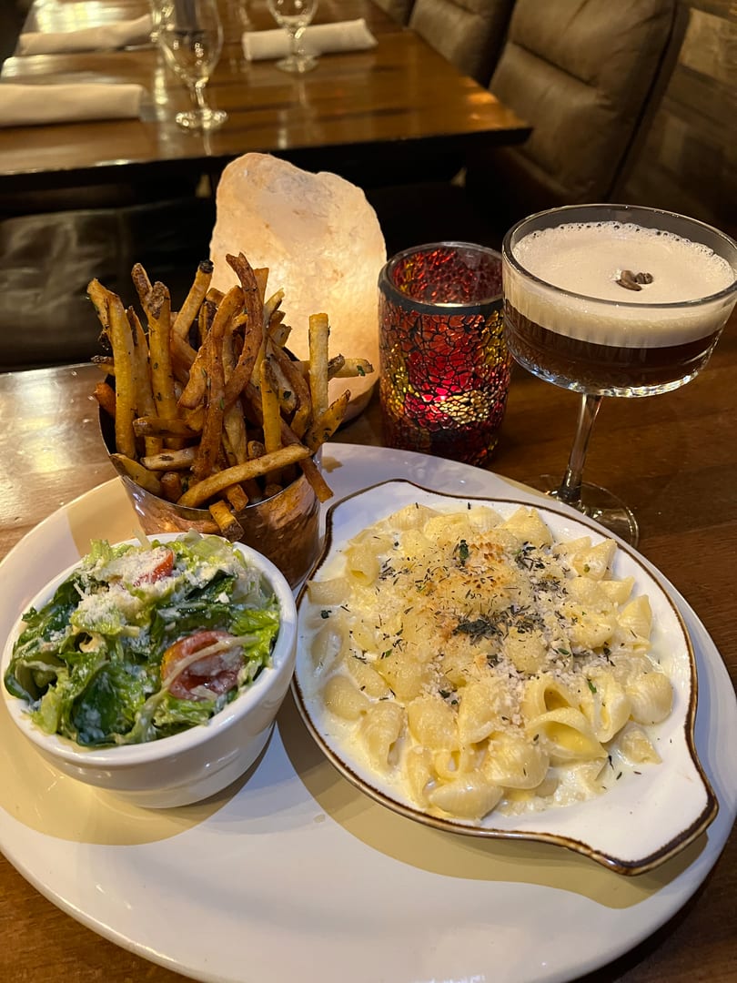 Creamy mac and cheese, crispy fries, fresh salad, and a cocktail on a cozy restaurant table.