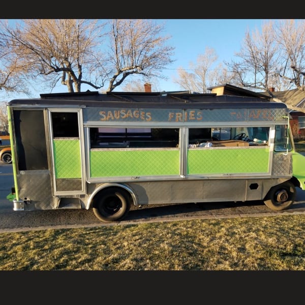 Gray and lime green food truck with 'SAUSAGES FRIES' on the side, parked on grass.
