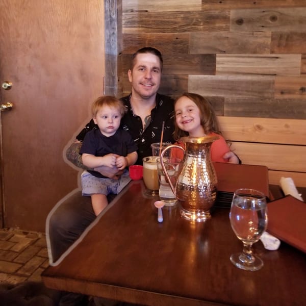 A man holding a baby and a young girl smiling at a restaurant table with drinks.