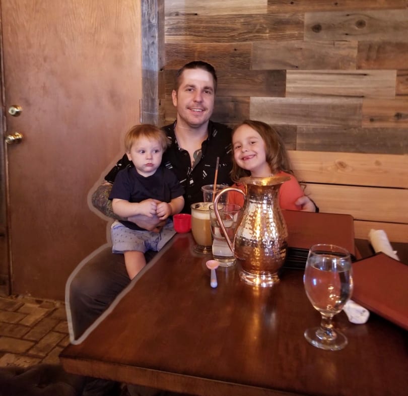 A man holding a baby and a young girl smiling at a restaurant table with drinks.