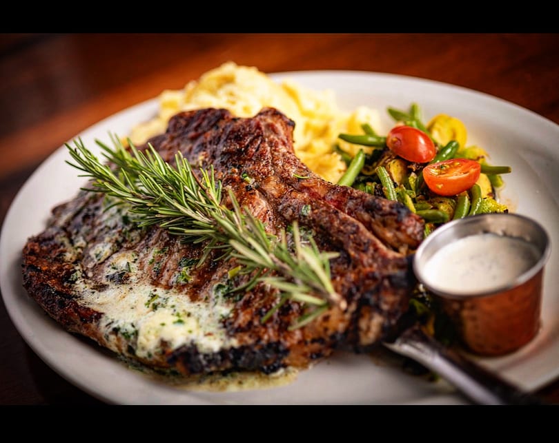 Juicy grilled steak with rosemary, mashed potatoes, roasted vegetables, and creamy sauce.