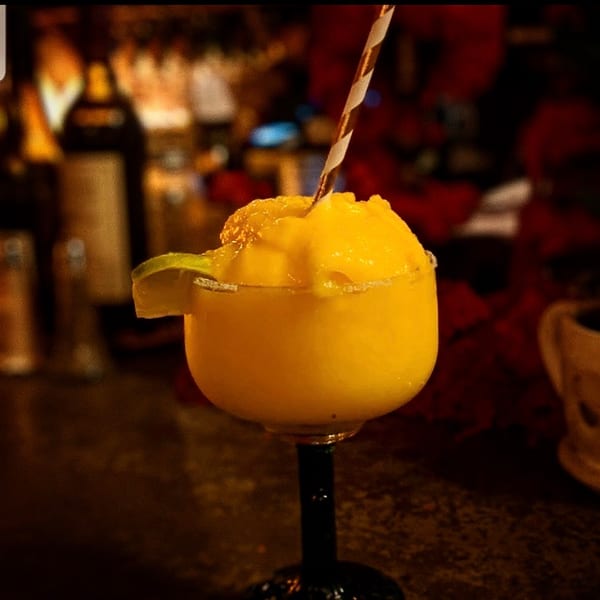 Frozen yellow margarita with a lime and striped straw at a dimly lit bar.
