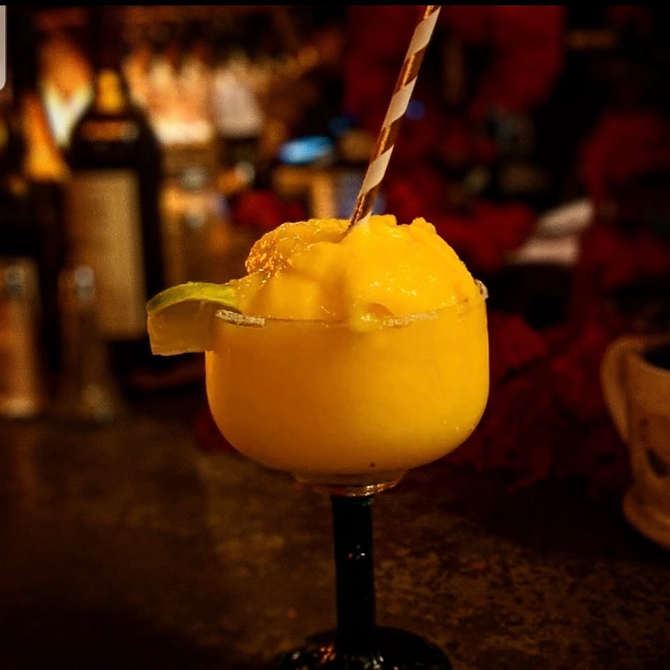 Frozen yellow margarita with a lime and striped straw at a dimly lit bar.