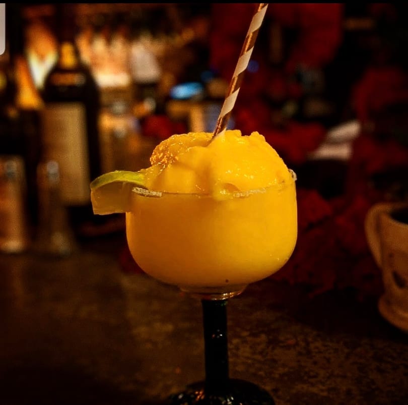 Frozen yellow margarita with a lime and striped straw at a dimly lit bar.