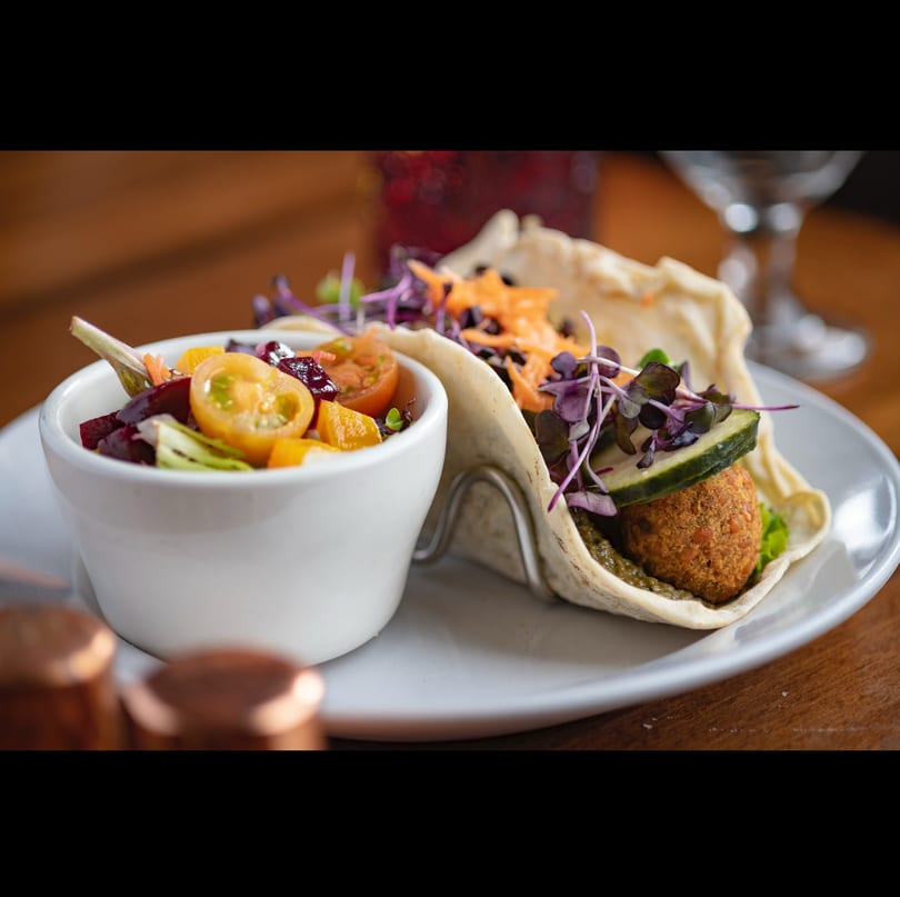 Fresh falafel tacos with cucumber, microgreens, and a colorful side salad on a white plate.