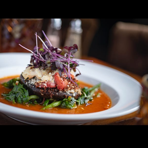 Stuffed portobello mushroom with quinoa, red peppers, and microgreens in a vibrant red sauce.
