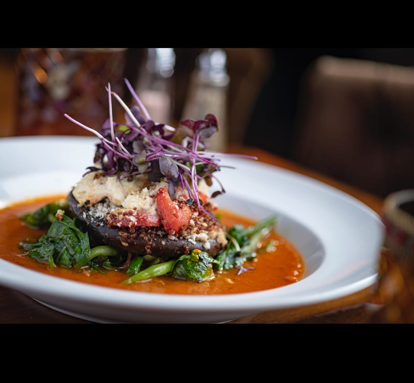 Stuffed portobello mushroom with quinoa, red peppers, and microgreens in a vibrant red sauce.