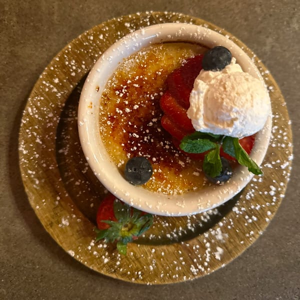 Caramelized creme brulee with whipped cream, strawberries, blueberries, and mint on a wooden plate.
