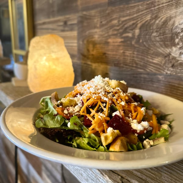 Colorful salad with mixed greens, shredded carrots, beets, feta, and croutons on a rustic wooden surface.