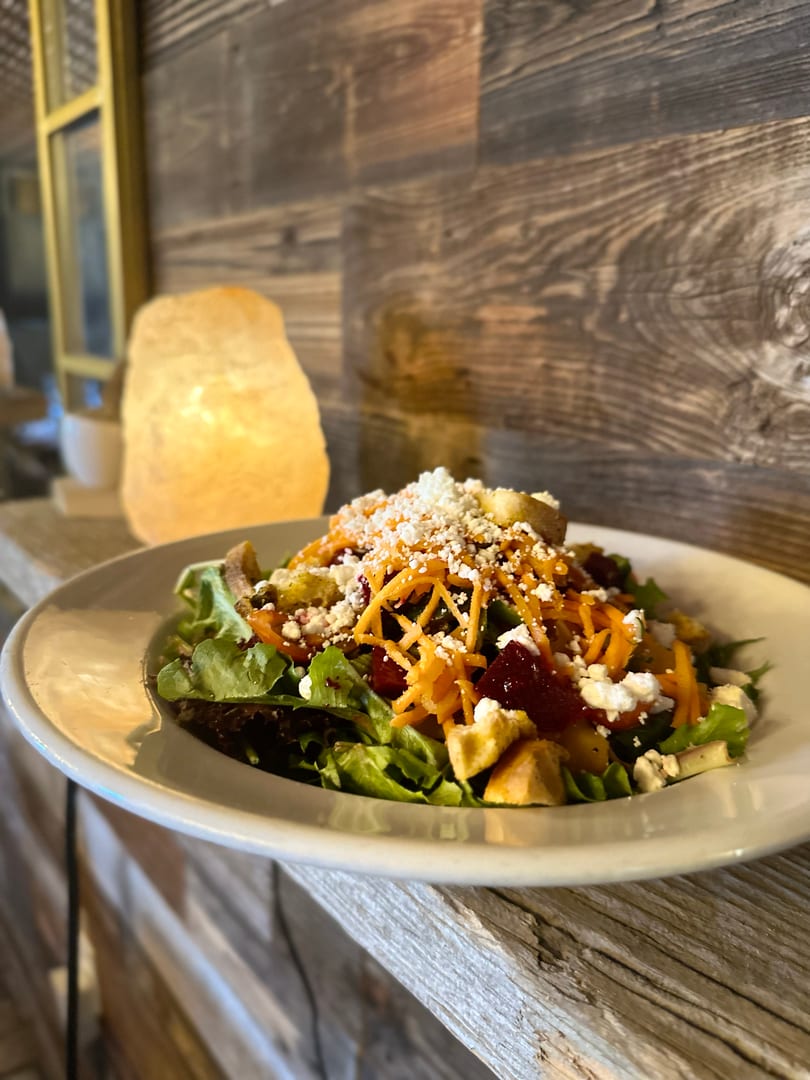 Colorful salad with mixed greens, shredded carrots, beets, feta, and croutons on a rustic wooden surface.