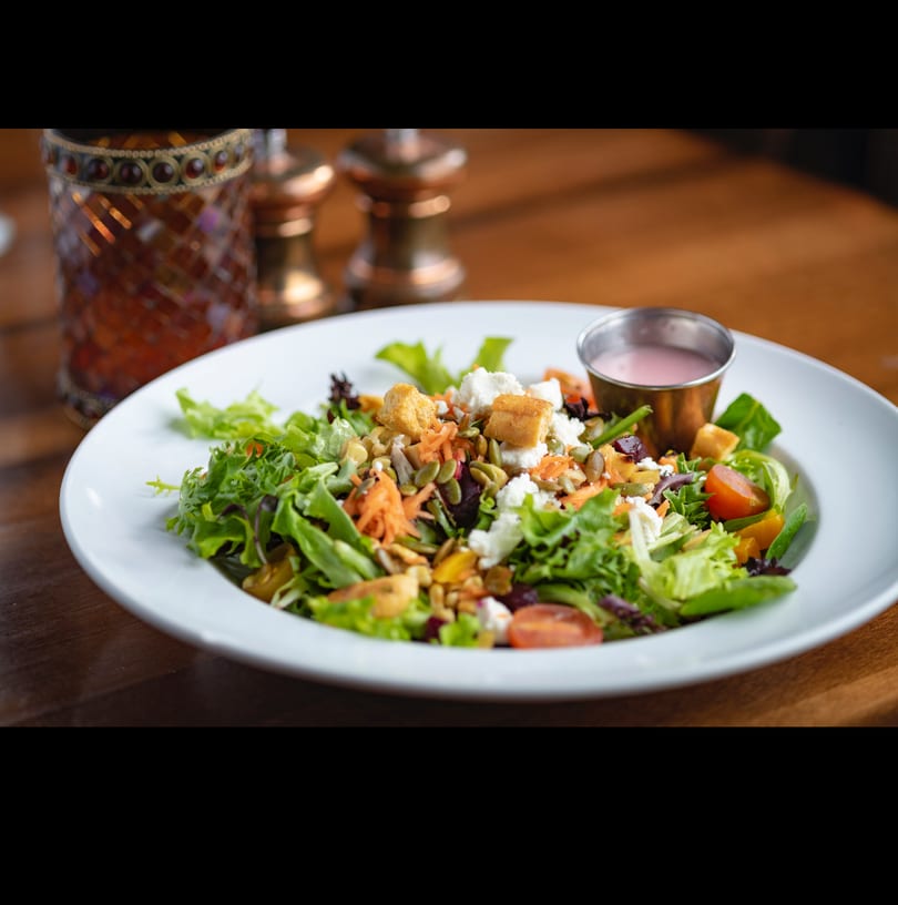 Fresh garden salad with feta, croutons, seeds, and cherry tomatoes, served with pink dressing.