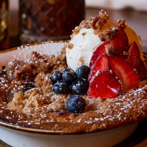 Baked dessert with vanilla ice cream, fresh strawberries, blueberries, and powdered sugar in a bowl.