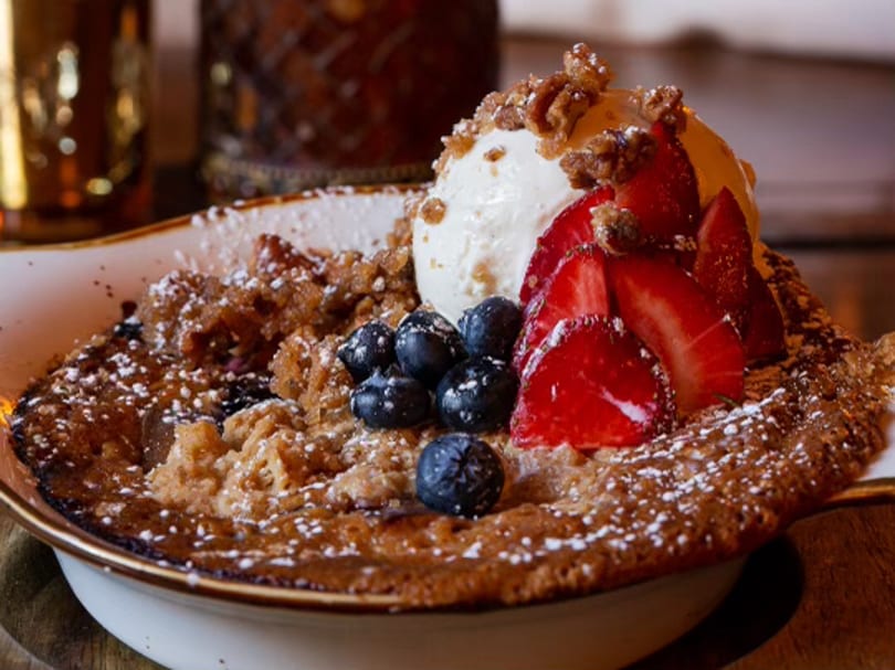 Baked dessert with vanilla ice cream, fresh strawberries, blueberries, and powdered sugar in a bowl.