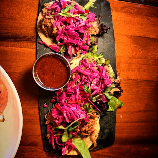 Overhead view of three tacos with pulled pork, vibrant purple cabbage, and dipping sauce.
