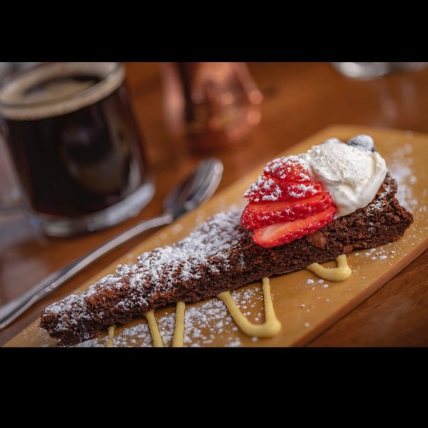 Decadent chocolate cake slice with fresh strawberries, whipped cream, and powdered sugar, next to coffee.
