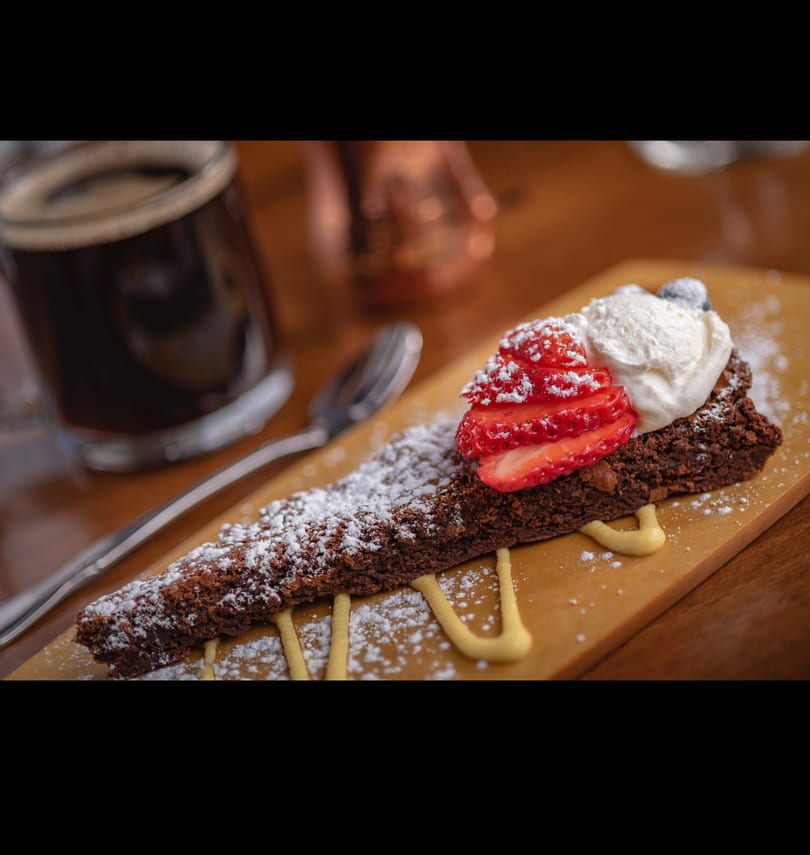 Decadent chocolate cake slice with fresh strawberries, whipped cream, and powdered sugar, next to coffee.