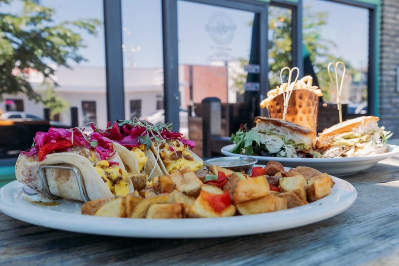 Plates of breakfast tacos, home fries, and a sandwich with fries on an outdoor restaurant patio.