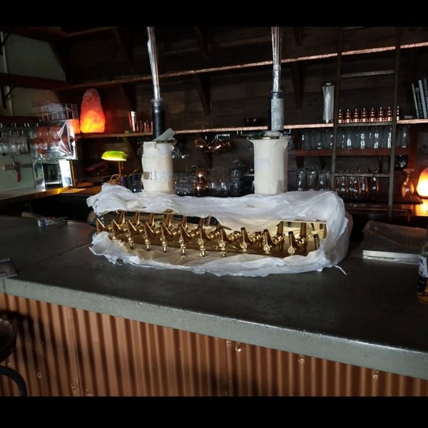 New golden beer tap system on a rustic bar counter with shelves of glasses and ambient lighting.