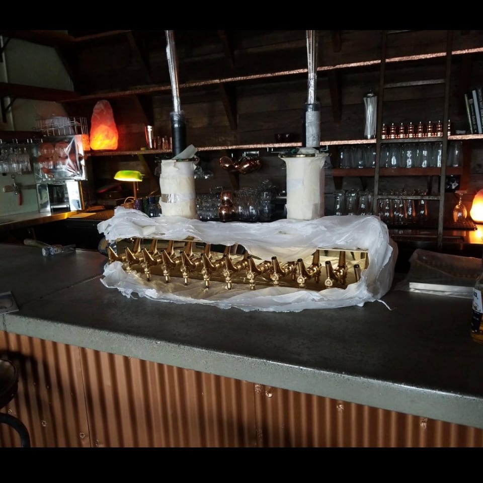 New golden beer tap system on a rustic bar counter with shelves of glasses and ambient lighting.