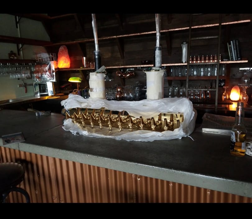 New golden beer tap system on a rustic bar counter with shelves of glasses and ambient lighting.