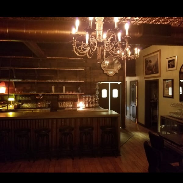 Elegant, dimly lit bar area featuring a large chandelier, wooden counter, and glassware.