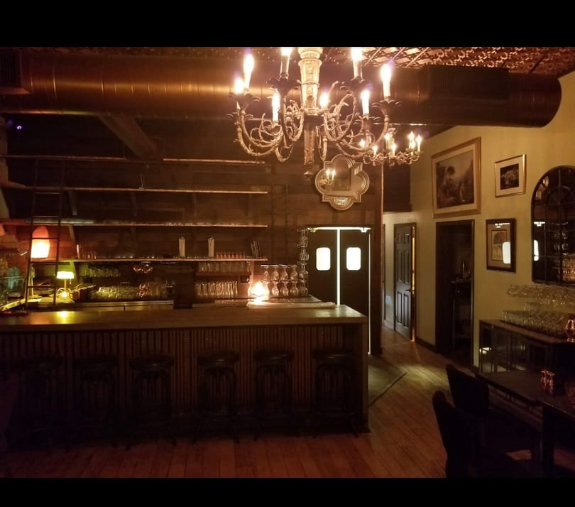 Elegant, dimly lit bar area featuring a large chandelier, wooden counter, and glassware.