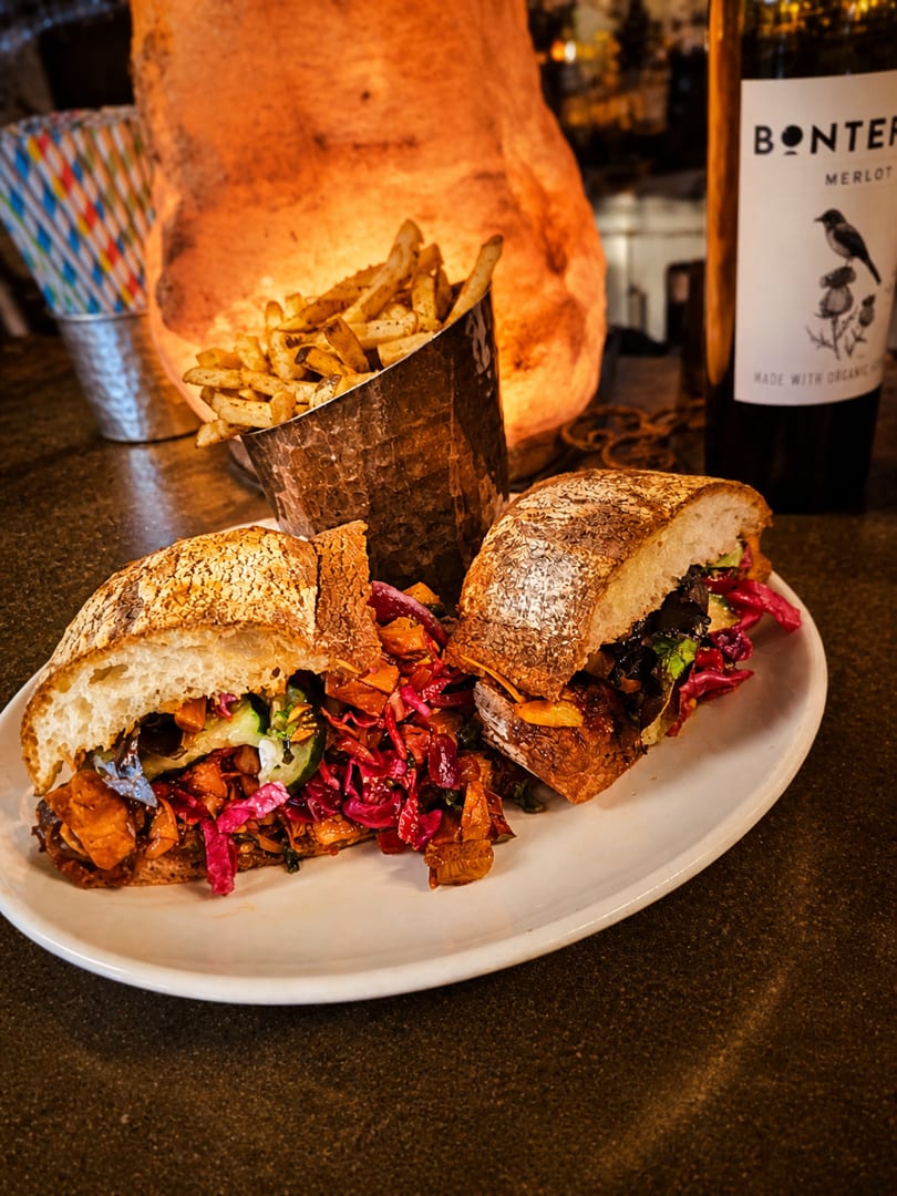 Hearty sandwich with red cabbage and fries, next to a Bonterra Merlot bottle.