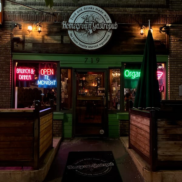 Homegrown Gastropub's illuminated exterior at night, featuring neon signs and outdoor dining barriers.