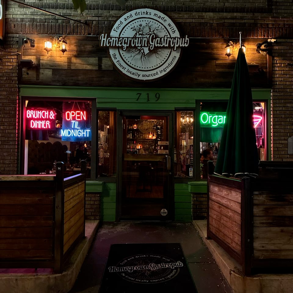 Homegrown Gastropub's illuminated exterior at night, featuring neon signs and outdoor dining barriers.