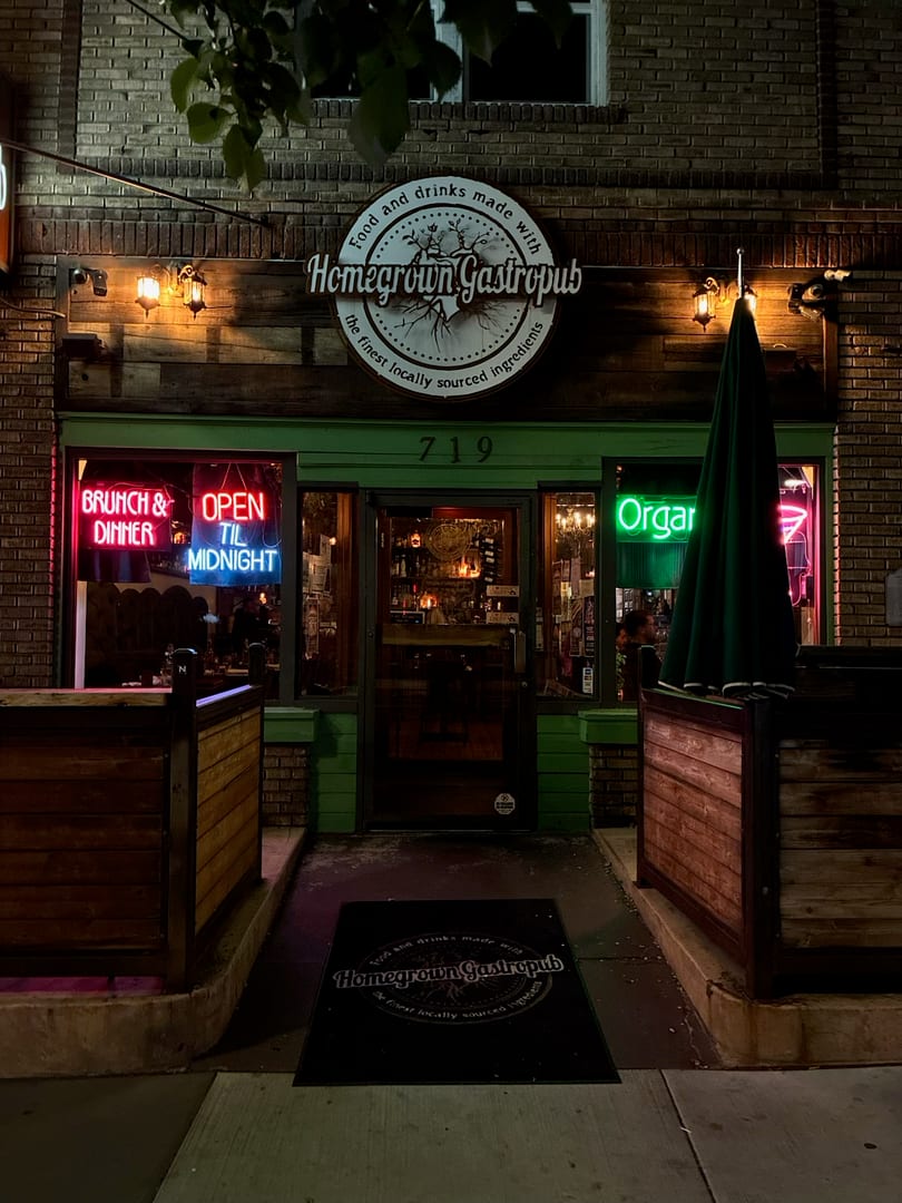 Homegrown Gastropub's inviting exterior at night, illuminated by neon signs and warm lights.