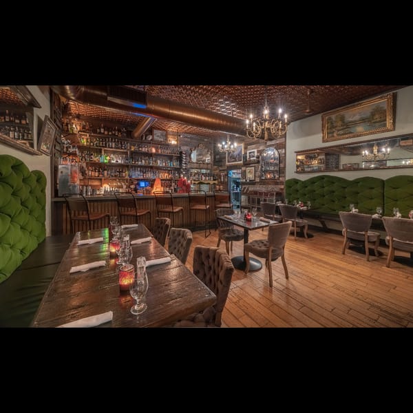 Cozy restaurant interior featuring a well-stocked bar, wooden tables, and plush green booth seating.