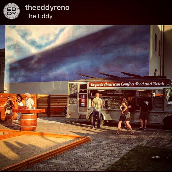 The Eddy's outdoor area with people, an "Organic American Comfort Food" truck, and a cloud mural.