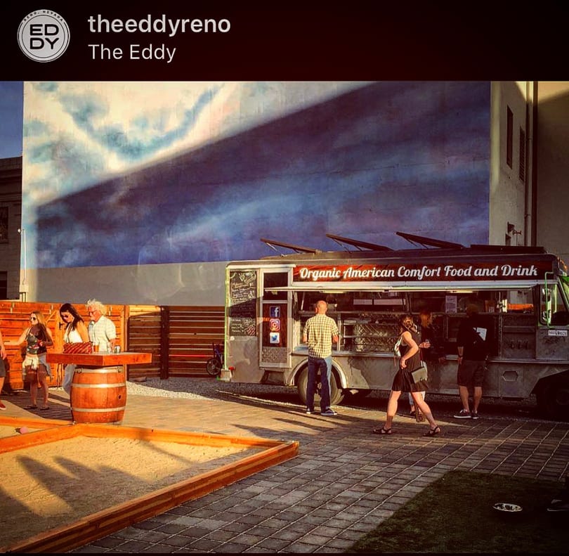 The Eddy's outdoor area with people, an "Organic American Comfort Food" truck, and a cloud mural.